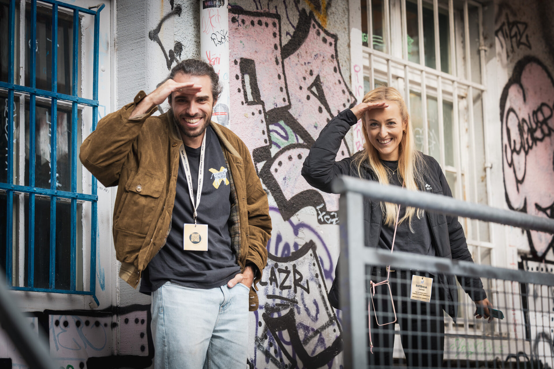 Zwei Lachende vor der Graffitiwand der Photobastei halten die Hand wie zum Ausschauen an die Stirn