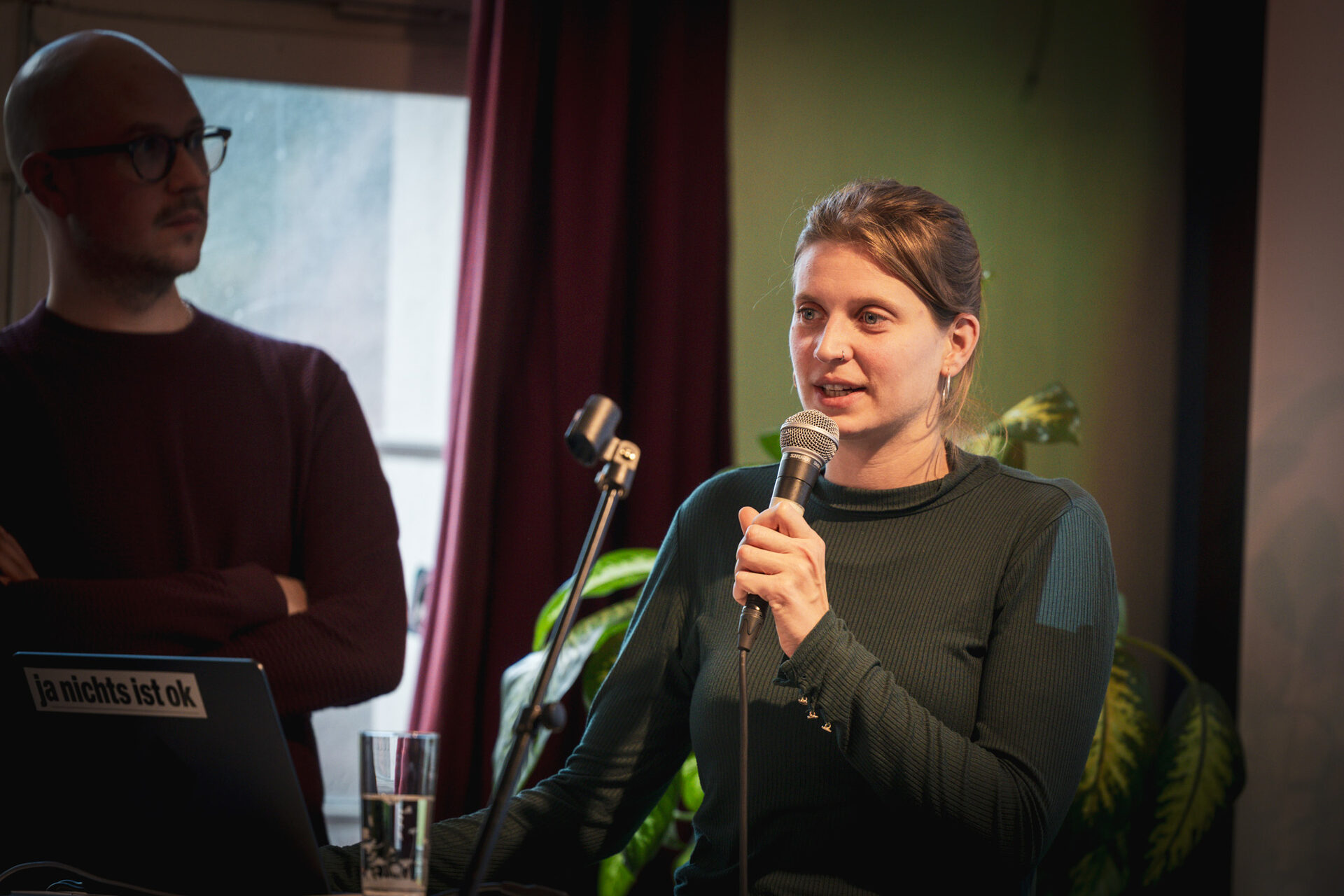 Anna Schubert spricht ins Mikrofon, neben ihr hört Hendrik Hassel zu